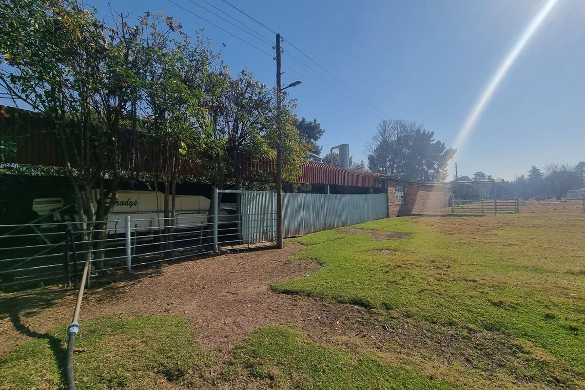 Exterior view of farm outbuildings featuring corrugated metal roofing, perimeter fencing, and open grazing land.
