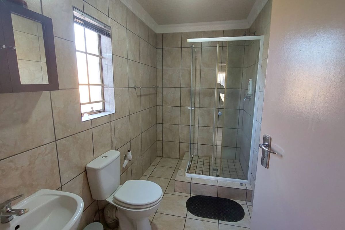 A functional bathroom featuring floor-to-ceiling wall tiles, a glass-enclosed shower, a pedestal basin, and a standard toilet.
