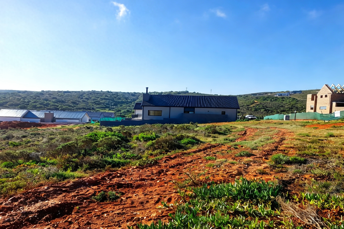 A wide-angle view of a residential property under construction, featuring a modern house with a metal roof set against a natural landscape.