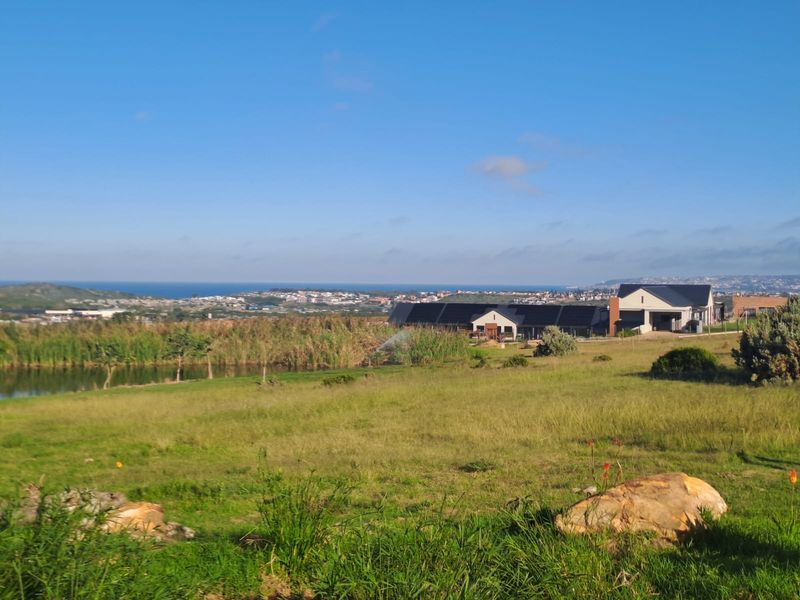 A scenic landscape view featuring a pond, open green space, and a modern residential property with solar panels in the distance.