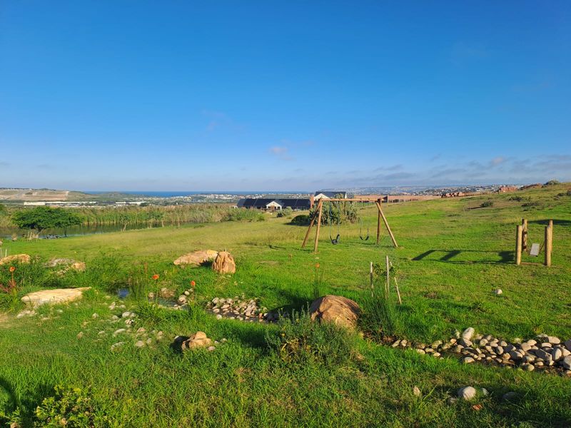 A scenic view of a landscaped garden featuring a natural pond, rockery, and expansive green space with distant coastal views.