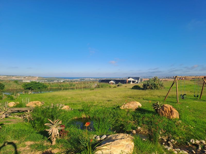 A scenic outdoor view featuring a landscaped garden with a natural pond, rock features, and expansive open green space overlooking the distant landscape.