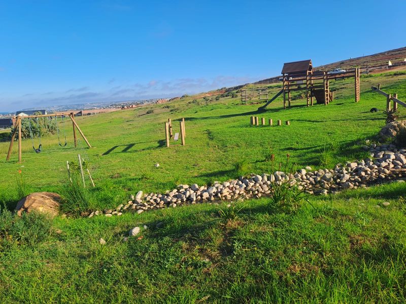 A spacious, well-maintained garden area featuring a wooden playground set and a decorative rock-lined drainage feature set against a scenic landscape.