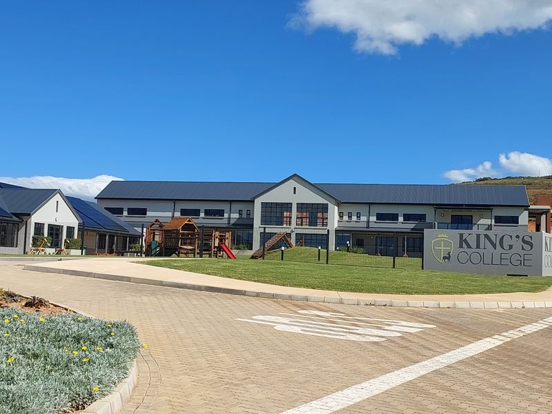 Front view of a modern school building featuring a paved driveway, well-maintained lawn, and contemporary architectural design with metal roofing.