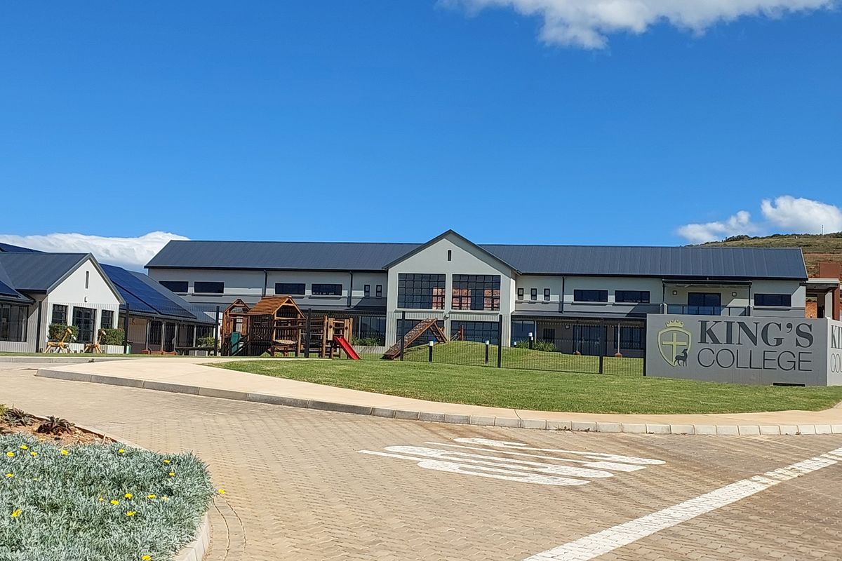 Front view of a modern school building featuring a paved driveway, well-maintained lawn, and contemporary architectural design with metal roofing.