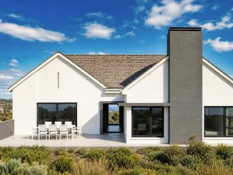 Rear elevation of a modern house featuring a paved patio, large sliding glass doors, and a prominent chimney, set against a landscaped garden.