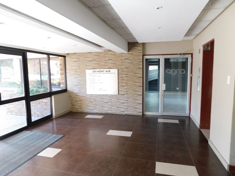A bright and professional office building entrance lobby featuring tiled flooring, a stone-clad feature wall, and large glass windows providing natural light.