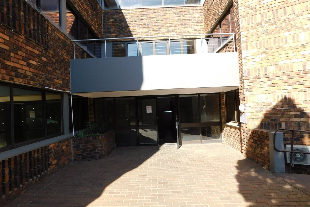 A view of the rear exterior courtyard of the office building, featuring brick masonry, a paved ground area, and a metal-railed balcony above the entrance.
