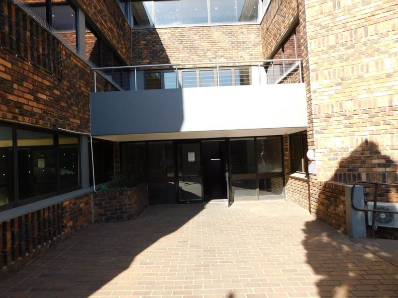 A view of the rear exterior courtyard of the office building, featuring brick masonry, a paved ground area, and a metal-railed balcony above the entrance.