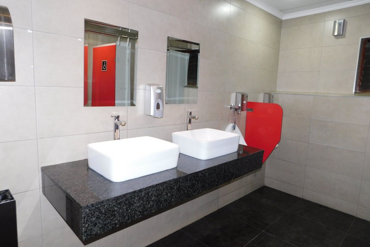 A modern commercial bathroom featuring a floating granite double vanity with vessel sinks, tiled walls, and a wall-mounted urinal.