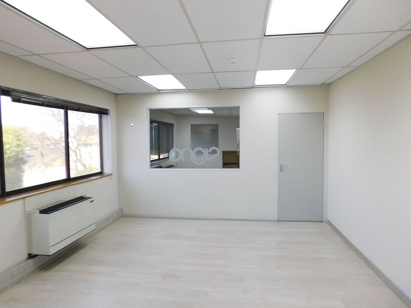 A bright, empty office space featuring a suspended ceiling, recessed lighting, laminate flooring, and an internal glass partition for a modern, professional look.