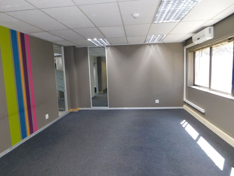 A vacant office space featuring a suspended ceiling, recessed lighting, split-system air conditioning, and carpeted flooring with a modern accent wall.