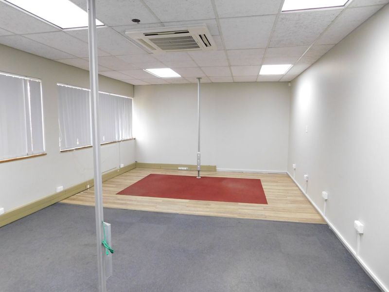 A vacant office space featuring a suspended ceiling, integrated air conditioning, and a mix of carpet and wood-look flooring.