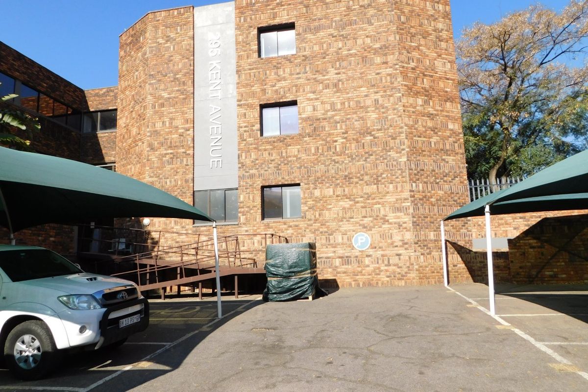 Exterior view of the office building facade featuring face brick construction, dedicated parking bays with shade cloth carports, and an accessible ramp entrance.