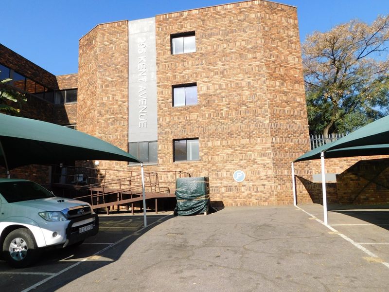 Exterior view of the office building facade featuring face brick construction, dedicated parking bays with shade cloth carports, and an accessible ramp entrance.