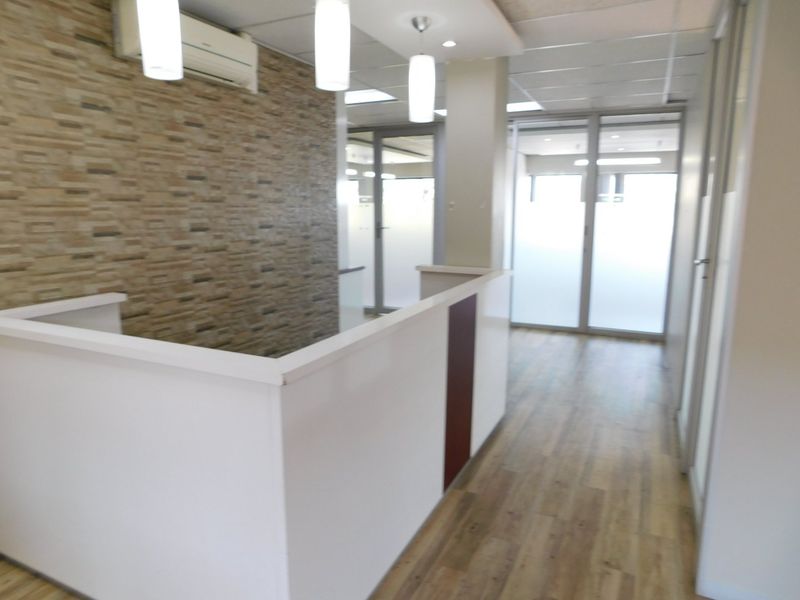 A bright, open-plan office space featuring a stone-cladding accent wall, modern pendant lighting, glass partitions, and durable laminate flooring.