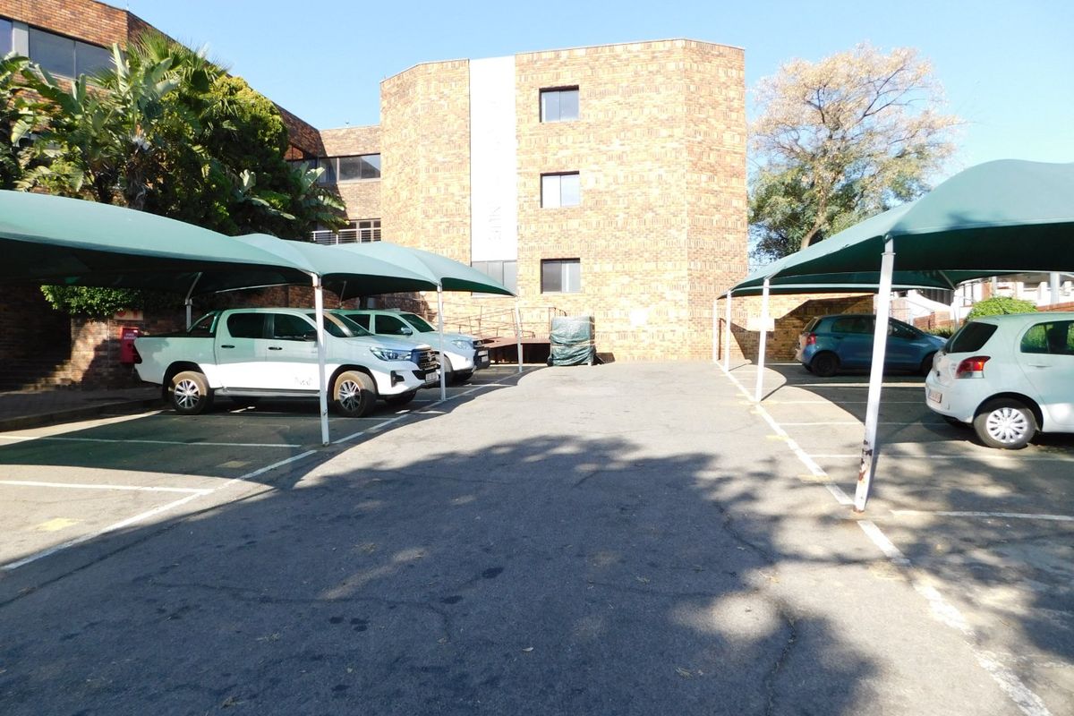 Exterior view of the office building parking area featuring asphalt paving and covered shade cloth parking bays.
