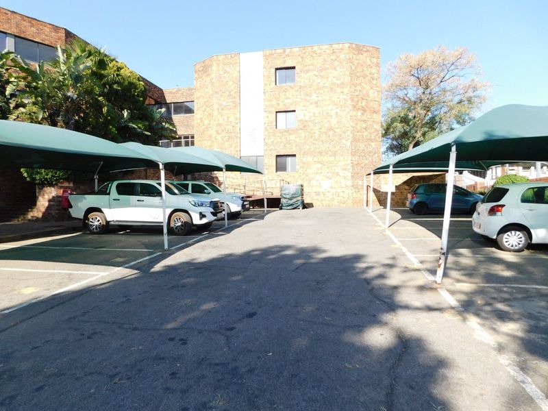Exterior view of the office building parking area featuring asphalt paving and covered shade cloth parking bays.