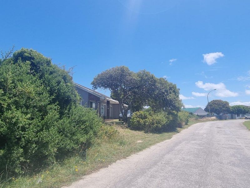 A street view of the residential property showing the paved road, boundary fencing, and established trees surrounding the site.