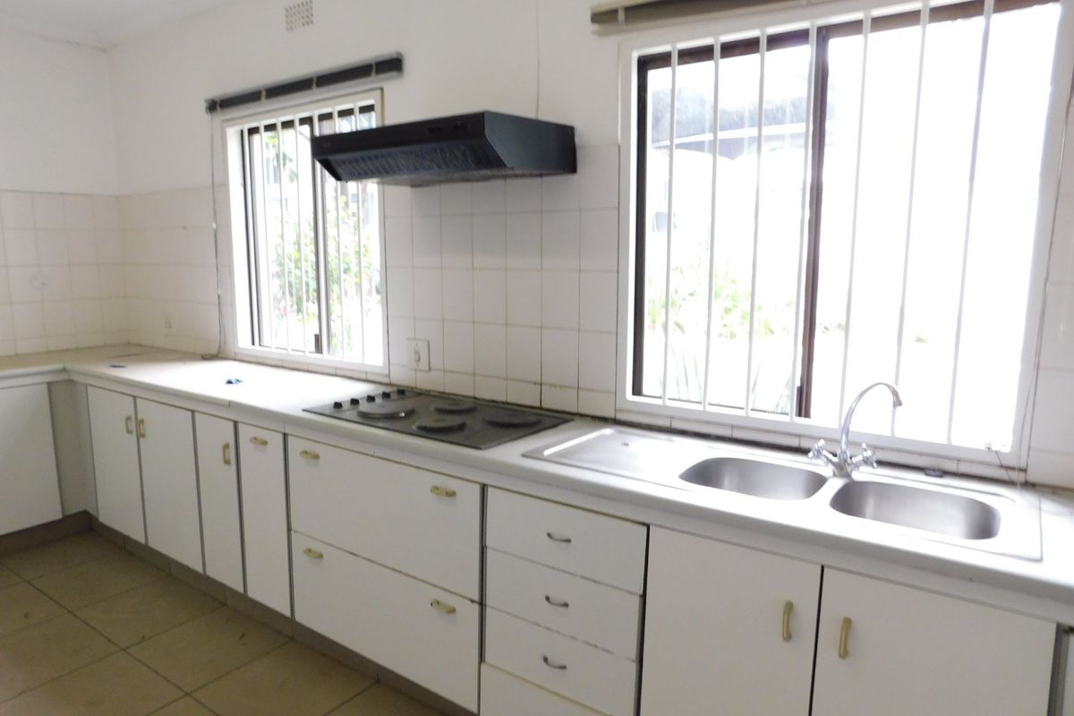 A functional kitchen featuring white cabinetry, a built-in hob, an extractor fan, and a double stainless steel sink with security bars on the windows.