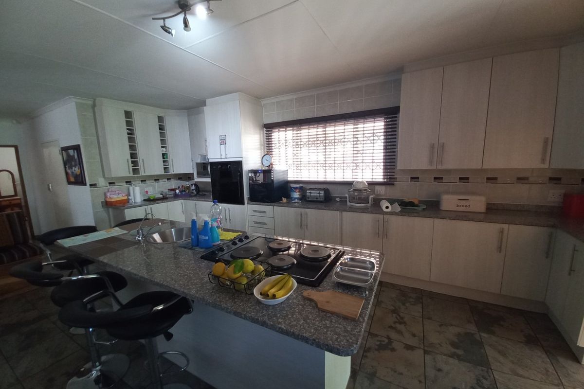 Spacious kitchen featuring light-toned cabinetry, granite countertops, a central island with a built-in hob, and tiled flooring throughout.