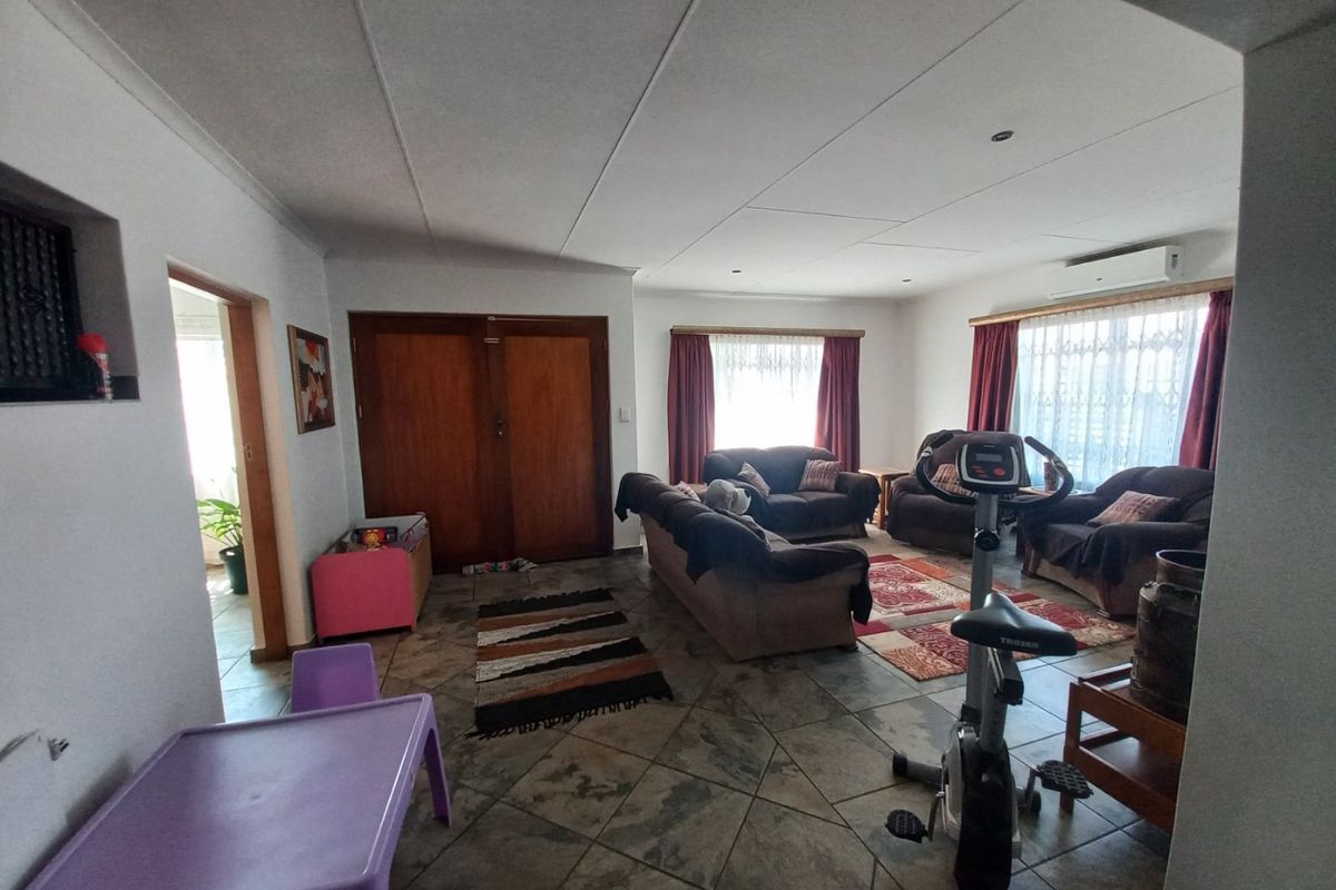 Spacious living area featuring tiled flooring, large windows with curtains, and a wall-mounted air conditioning unit.