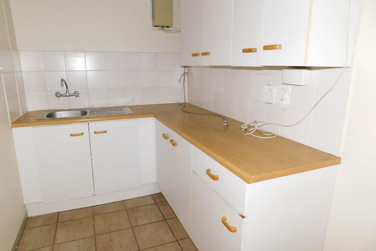 A functional kitchenette featuring white cabinetry, wood-look laminate countertops, a stainless steel sink, and tiled splashbacks in an office setting.