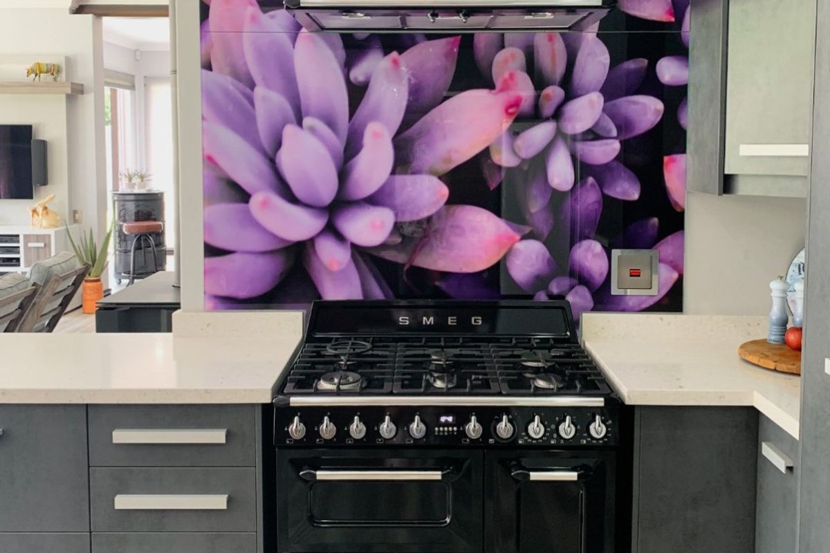 Modern kitchen featuring a high-end Smeg freestanding oven, matching extractor fan, and a striking floral-patterned glass splashback with stone countertops.