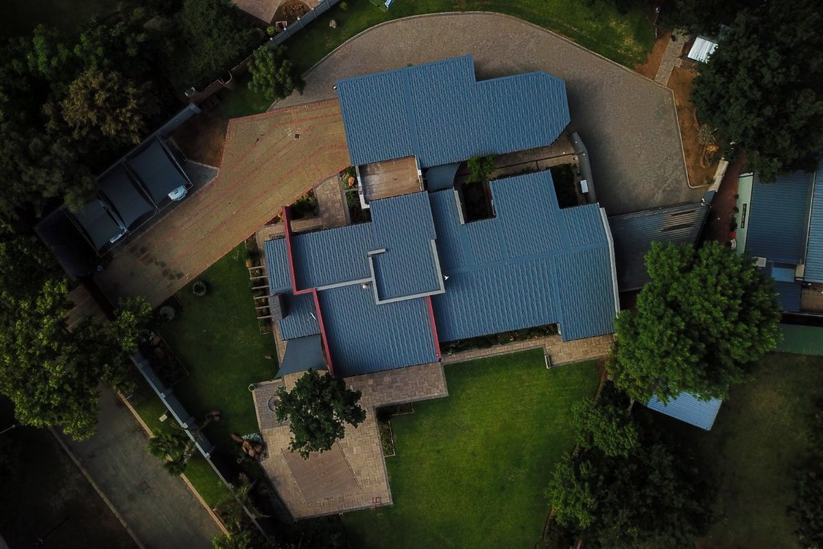 Aerial view of the property showcasing the expansive roof structure, paved driveway, landscaped garden, and swimming pool area.