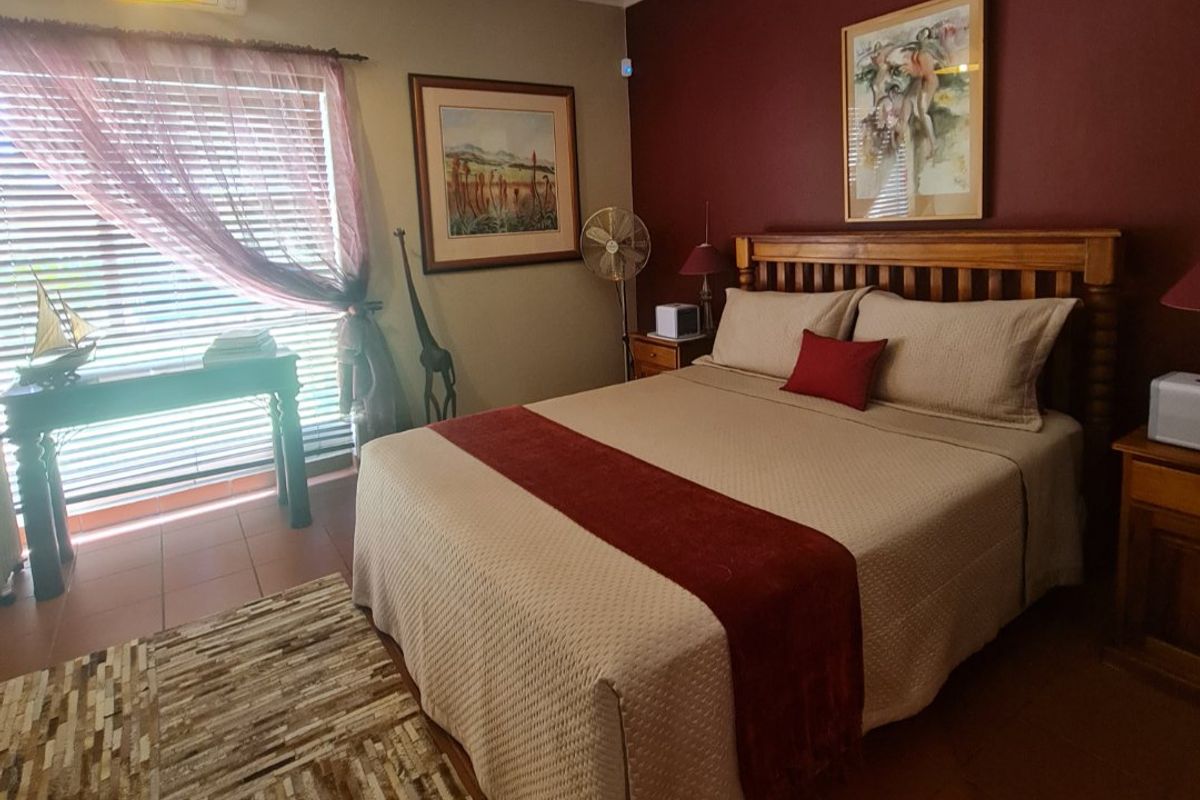 A well-maintained bedroom featuring tiled flooring, a wall-mounted air conditioning unit, and a large window with fitted blinds.