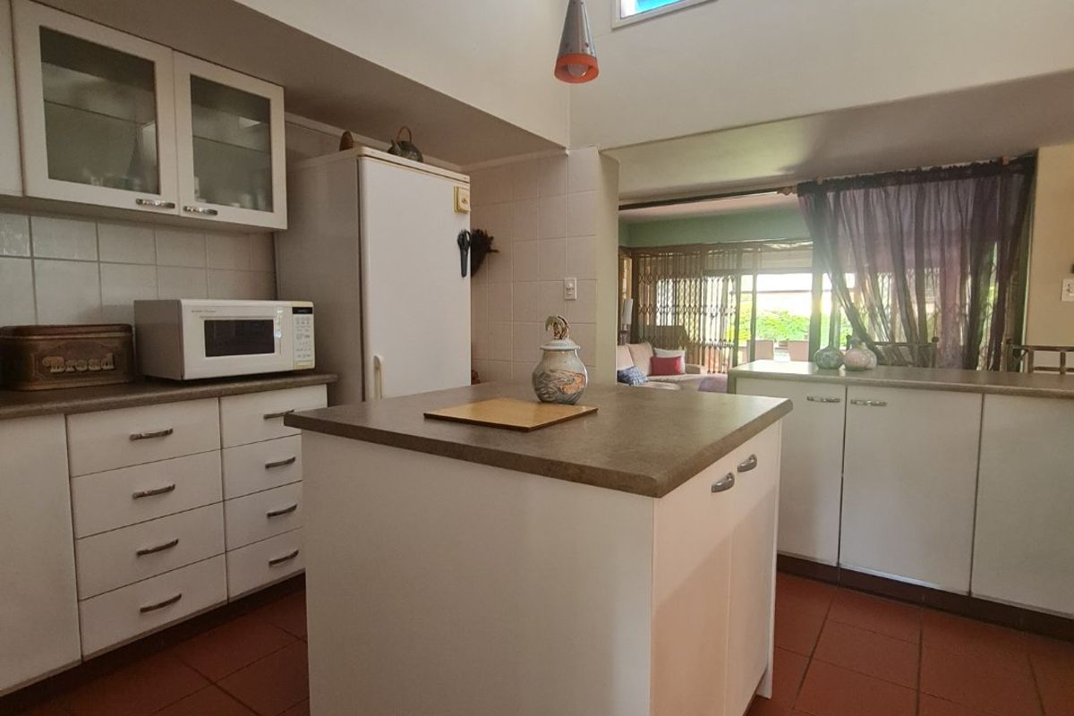 A functional kitchen featuring white cabinetry, a central island, and high-level windows that provide natural light, connecting to an adjacent living area.