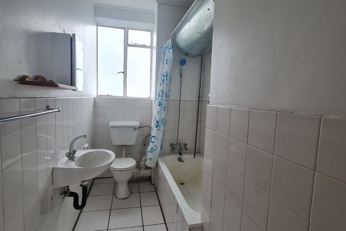 A dated bathroom featuring a standard bathtub with shower attachment, wall-mounted basin, and toilet, finished with white ceramic wall and floor tiles.