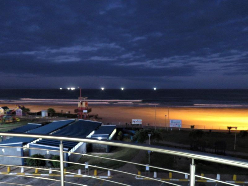 A night view overlooking the beach and coastline from a balcony with a stainless steel balustrade.