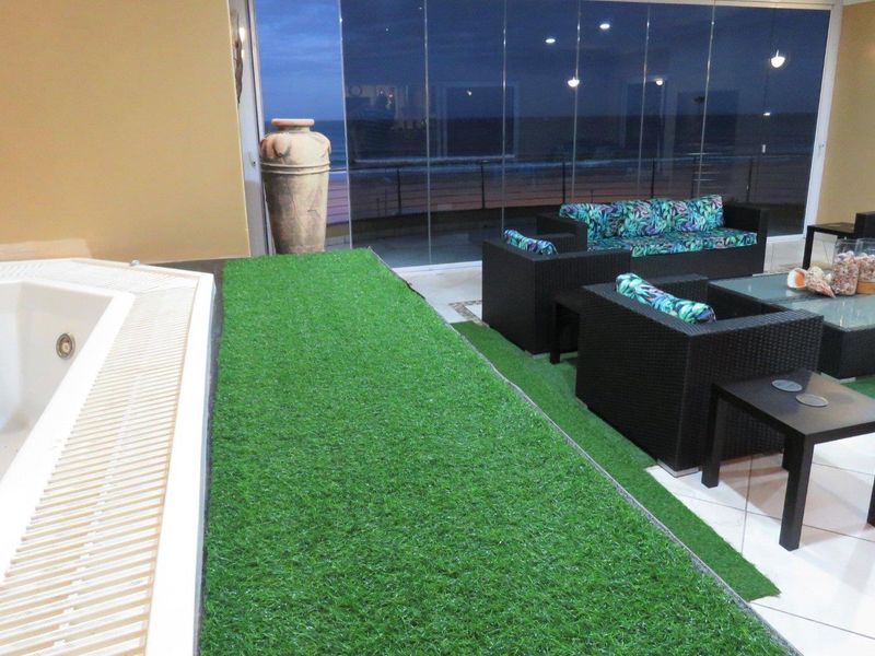 Covered balcony area featuring a built-in jacuzzi, artificial grass flooring, and large glass sliding doors offering an outdoor view.