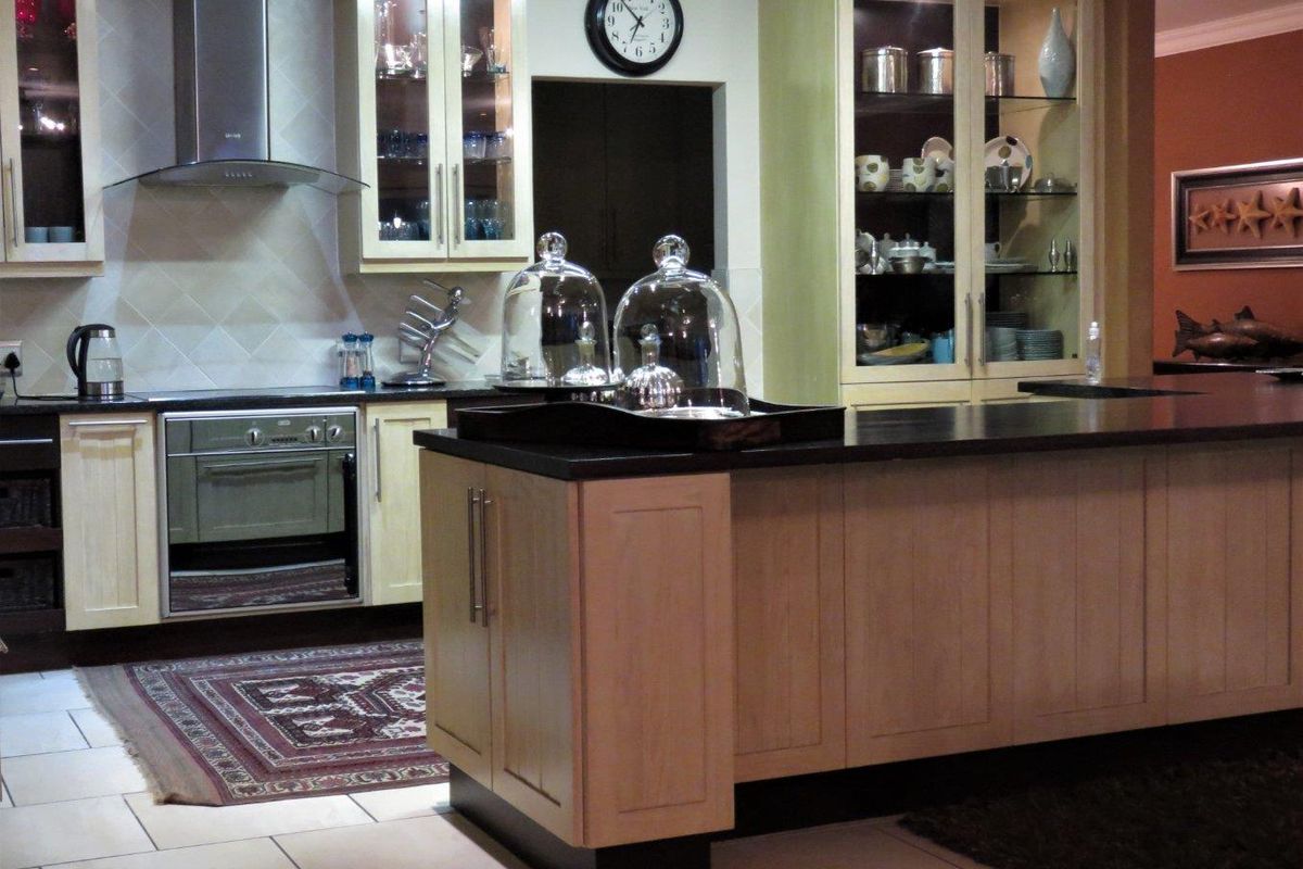 A well-appointed kitchen featuring light wood cabinetry, a central island with dark stone countertops, built-in oven, and elegant glass-front display units.