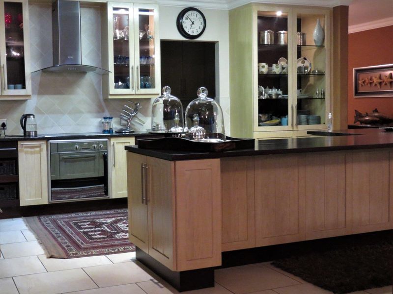 A well-appointed kitchen featuring light wood cabinetry, a central island with dark stone countertops, built-in oven, and elegant glass-front display units.
