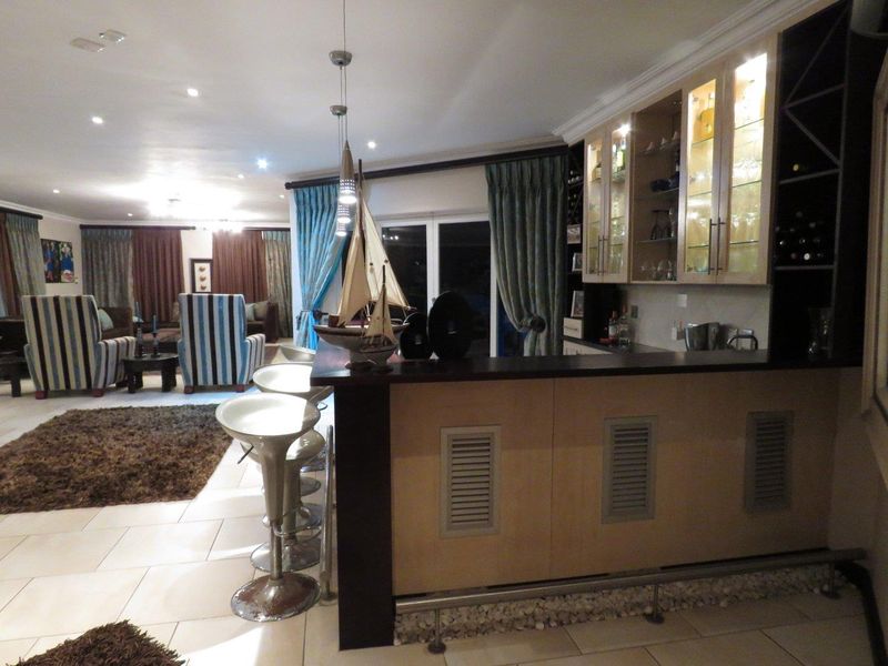 Open-plan living area featuring a built-in bar with glass-fronted cabinetry, recessed lighting, and tiled flooring, seamlessly connecting to the main lounge space.