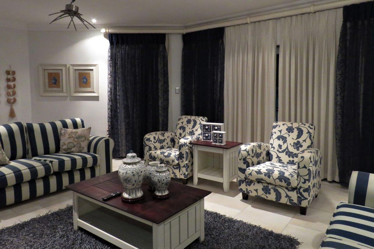 A comfortable living room featuring tiled flooring, recessed lighting, and large windows dressed with layered curtains.