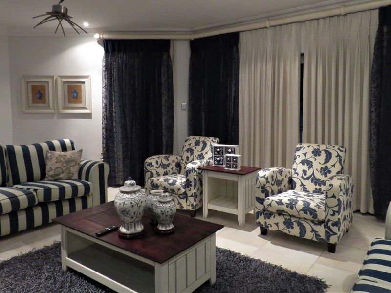 A comfortable living room featuring tiled flooring, recessed lighting, and large windows dressed with layered curtains.