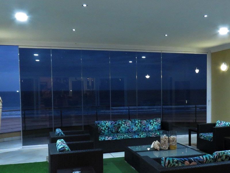 Spacious enclosed balcony featuring stacking glass doors, recessed lighting, and a built-in braai, offering panoramic ocean views.