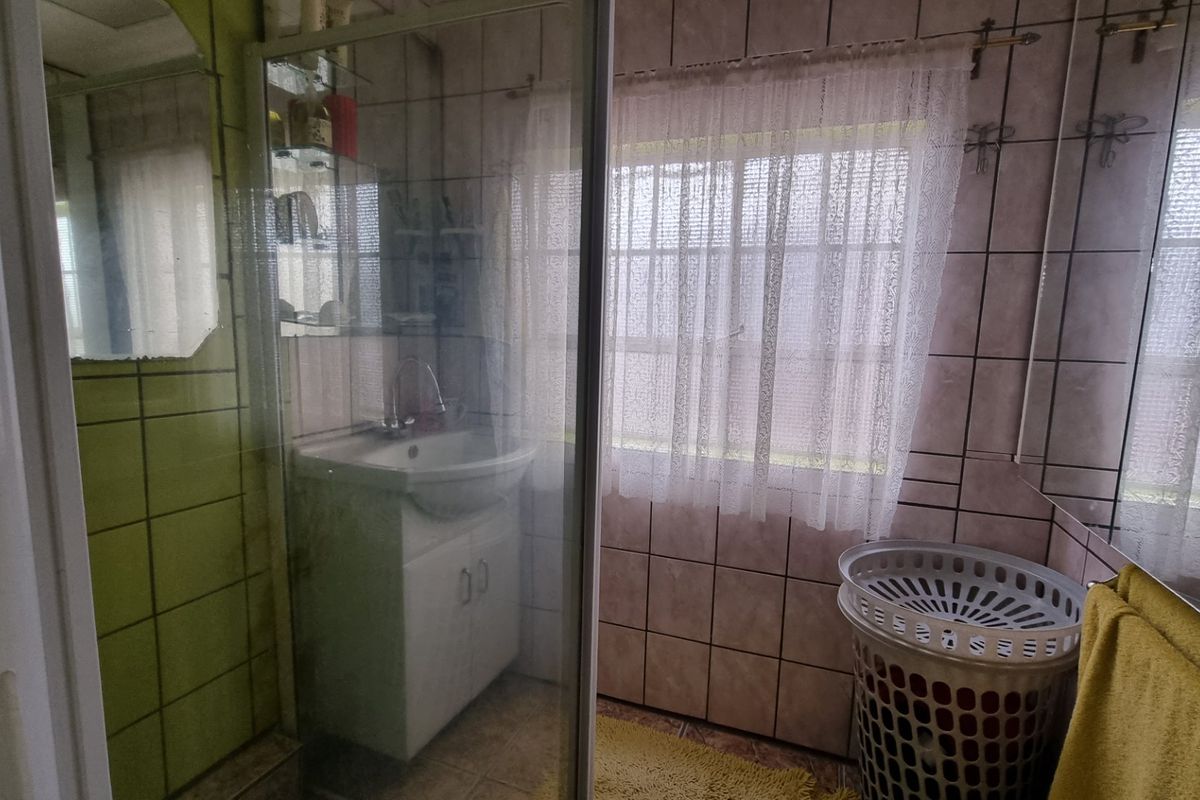A dated bathroom featuring a glass-enclosed shower, a vanity basin, and tiled walls throughout.