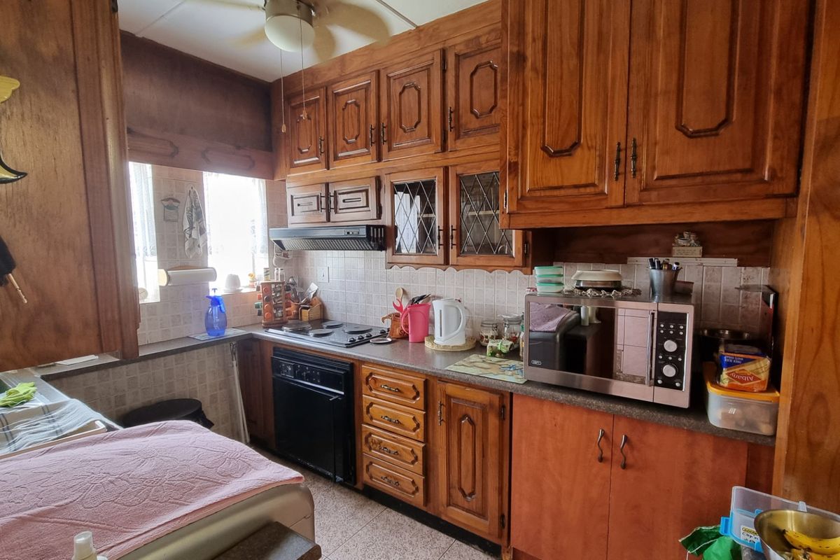 A dated kitchen featuring traditional wood cabinetry, a built-in oven, extractor fan, and tiled backsplash, offering a functional layout with potential for modernization.