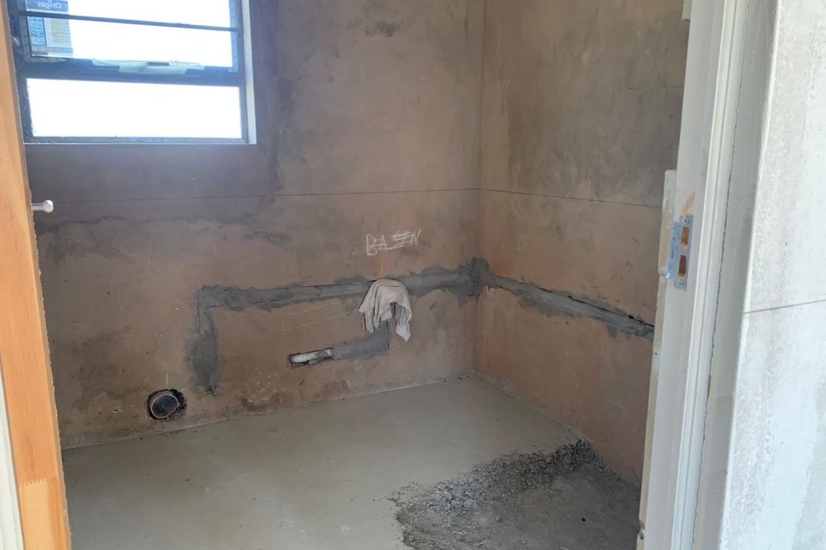 An unfinished bathroom space in shell condition, featuring exposed plumbing rough-ins and bare wall surfaces, ready for final tiling and fixture installation.