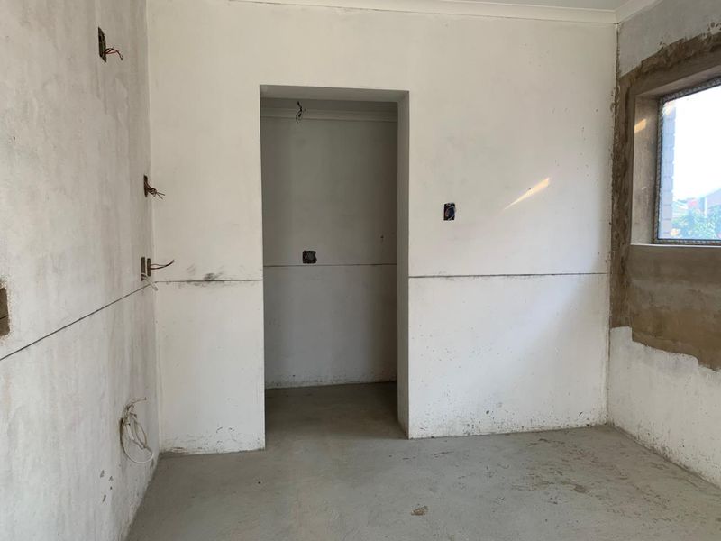 An unfinished bedroom space featuring exposed electrical wiring, concrete flooring, and unpainted plaster walls, offering a blank canvas for renovation.
