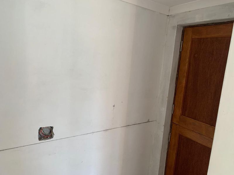 An unfinished interior space showing exposed electrical wiring and a timber door, requiring completion of wall finishes and electrical installation.