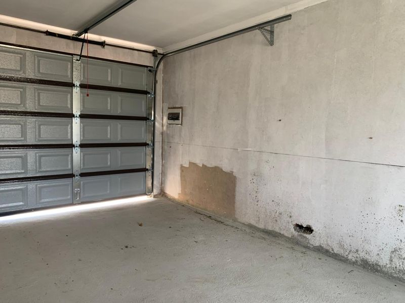 An empty garage space featuring a sectional door, showing visible wall plaster damage and damp staining requiring maintenance.