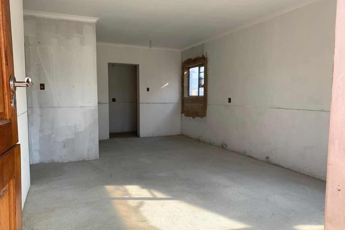 An empty, unfinished living area featuring bare concrete floors and unpainted plaster walls, awaiting final flooring and decorative finishes.