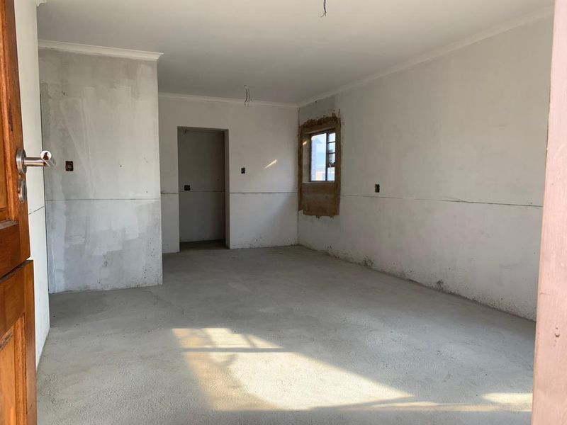An empty, unfinished living area featuring bare concrete floors and unpainted plaster walls, awaiting final flooring and decorative finishes.