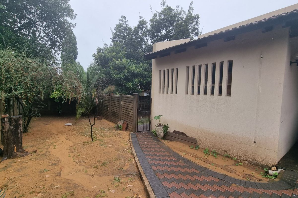 A view of the rear garden area featuring a paved walkway, perimeter fencing, and the side elevation of the house with vertical slit windows.