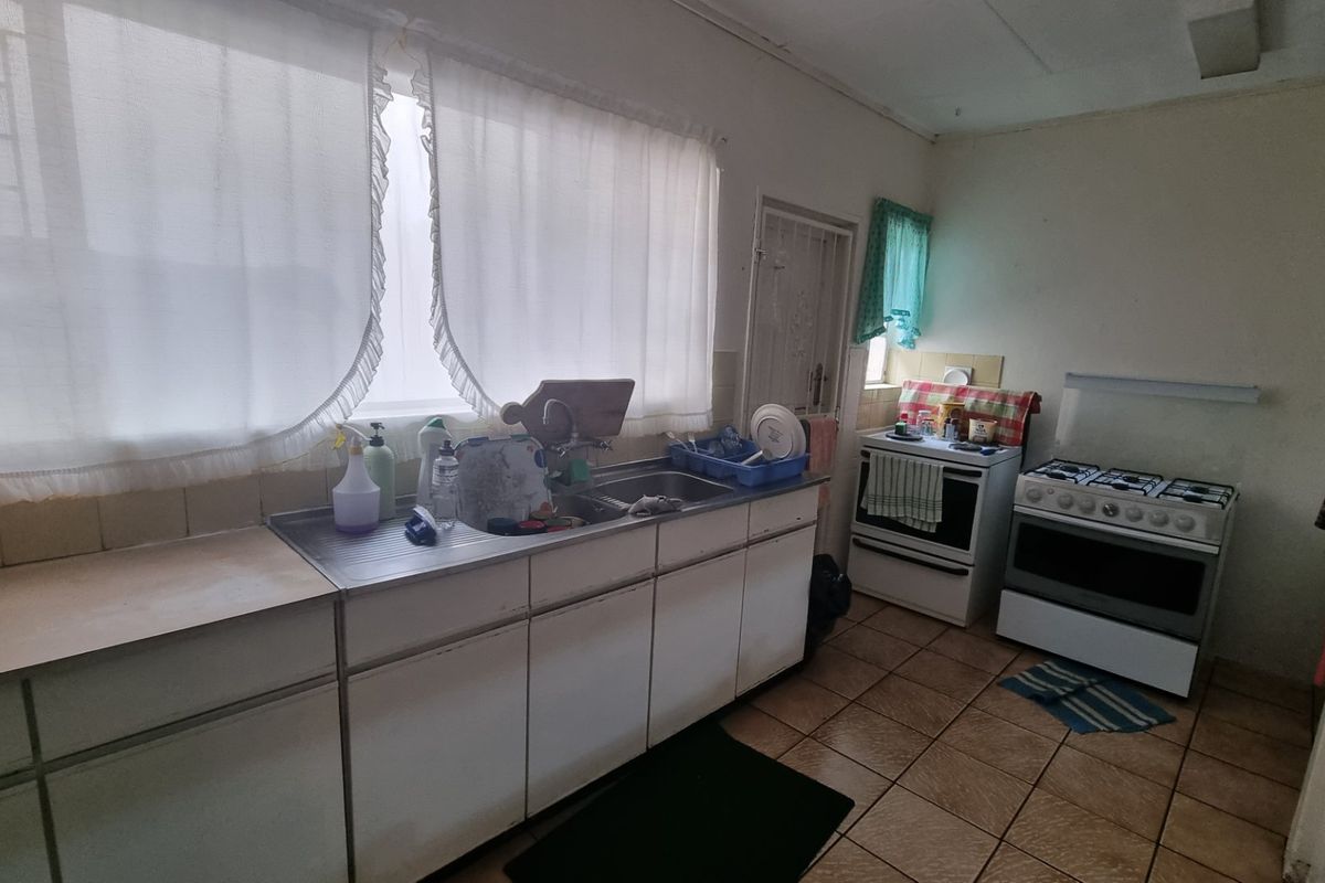 A functional kitchen featuring a stainless steel sink, tiled splashbacks, and space for a freestanding stove, offering potential for modernization.